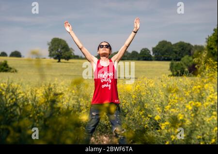 Young woman holding hands high up while enjoying the warm sunny day, positive vibes only vest top. Stockfoto