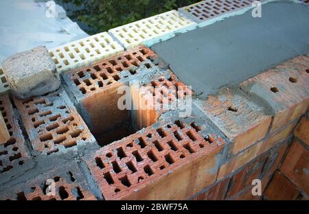 Ein Abgaskacht in einer Wand aus rotem Ziegel mit Zement gefüllt. Verkleidung mit gelben und braunen Ziegeln. Selektiver Fokus. Konzept der Konstruktion. Unvollendeter Hous Stockfoto