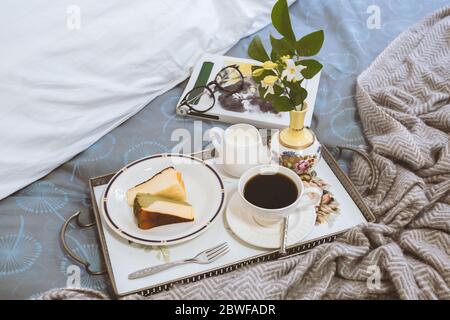 Frühstück im Bett Scheibe Cheesesescake mit Kaffeetasse und Lesebuch. Stockfoto