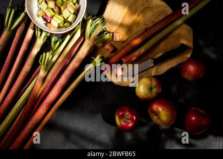 Frischer Rhabarber, Äpfel und Schneidebrett auf dunklem Hintergrund Stockfoto