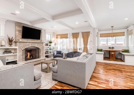 Ein gemütliches Wohnzimmer mit einem Fernseher über einem Kamin vor Sofas und Stühlen montiert. Eine Frühstücksecke ist ebenfalls im Haus eingebaut. Stockfoto