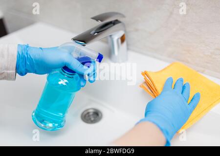 Weibliche Hände tragen Gummihandschuhe halten Mikrofasertuch und Sprühflasche Desinfektionsmittel Waschbecken im Badezimmer zu desinfizieren. Schutz vor Viren oder Bacter Stockfoto