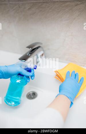Weibliche Hände tragen Gummihandschuhe halten Mikrofasertuch und Sprühflasche Desinfektionsmittel Waschbecken im Badezimmer zu desinfizieren. Stockfoto