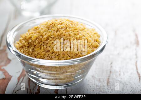 Ungekocht Bulgur in blauer Schüssel auf hölzernen Tisch Hintergrund. Trockene Bulgur. Verschüttete Bulgur Stockfoto