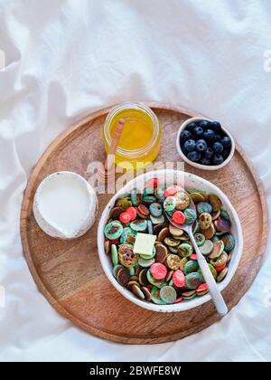 Trendige Speisen - Pfannkuchen Müsli. Schale mit bunten Mini-Cerealien-Pfannkuchen auf Holztablett über dem Bett. Kleine Pfannkuchen mit natürlicher Farbe - grüne Matcha, türkisfarbenes Spirulina, blaue Erbse, rote Fragon-Frucht Stockfoto