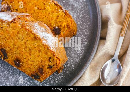 Grauer Teller mit zwei Stücken Karottenkuchen und Löffel auf beiger Serviette. Nahaufnahme Stockfoto