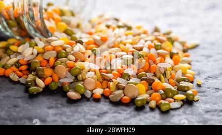 Bunte verschiedene Linsen und Vollkornsamen aus einem Glas auf dem Tisch gegossen Stockfoto