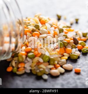 Bunte verschiedene Linsen und Vollkornsamen aus einem Glas auf dem Tisch gegossen Stockfoto