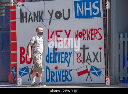 Eine Frau radelt an einem Plakat vorbei, das dem NHS und den Schlüsselarbeitern in Edinburgh dankt, da die Menschen Familie und Freunde im Freien treffen und wieder Sport wie Golf und Tennis spielen können, während Schottland in Phase eins des Plans der schottischen Regierung geht, die Sperre allmählich zu heben. Stockfoto