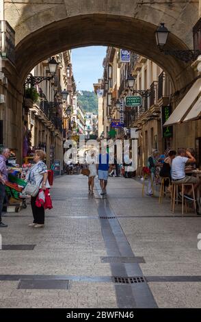 Touristen wandern und entspannen unter einer der vielen Bogenstraßen in San Sebastian, Spanien an einem hellen Sommertag Stockfoto