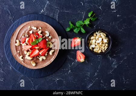 Eingeweichte Cashew-Basis Käsekuchen mit weißen und dunklen Schokolade Füllung und Kokosmilch und No-Bake Kruste aus Datteln, Kakao und Pekannüsse mit frischem Strohhalme Stockfoto