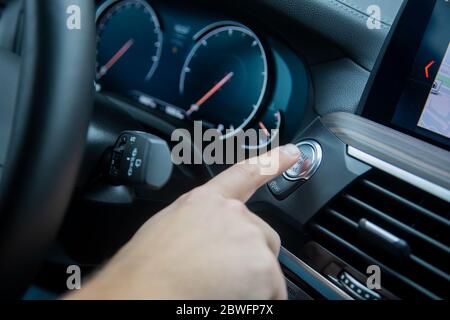 Männliche Finger drückt die Start-Stopp-Motor-Taste auf einem Auto Armaturenbrett. Nahaufnahme, Soft-Fokus, im Hintergrund das Armaturenbrett und Auto Tachometer in Unschärfe Stockfoto