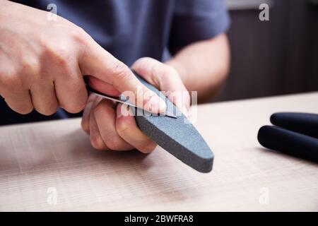 Nahaufnahme starke männliche Hände schärfen ein Küchenmesser mit einem Schleifstein. Heim Haushaltsmesser schärfen. Stockfoto