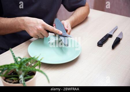 Nahaufnahme starke männliche Hände schärfen ein Küchenmesser mit einem Schleifstein. Heim Haushaltsmesser schärfen. Stockfoto