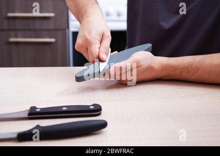 Nahaufnahme starke männliche Hände schärfen ein Küchenmesser mit einem Schleifstein. Heim Haushaltsmesser schärfen. Stockfoto