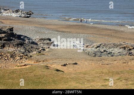 Ein Paar taucht während der Absperrung mit den Füßen in das eiskalte Wasser des Bristol-Kanals an diesem menschenleeren Strand. Stockfoto