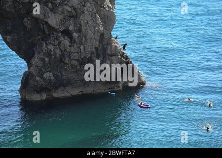 Die Menschen springen von Felsen über dem Meer in Durdle Door, nahe Lulworth, in Dorset, nachdem die Öffentlichkeit daran erinnert wurde, soziale Distanzierung nach der Lockerung der Beschränkungen der Coronavirus-Sperre in England zu praktizieren. Stockfoto