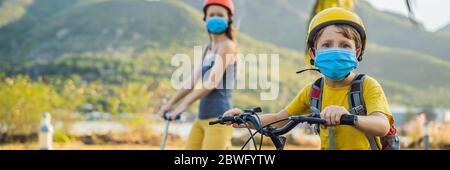 Aktive Schulkind und seine Mutter in medizinischen Maske und Schutzhelm Reiten ein Fahrrad mit Rucksack an sonnigen Tag. Fröhliches Kinderradeln auf dem Weg zur Schule. Sie Stockfoto