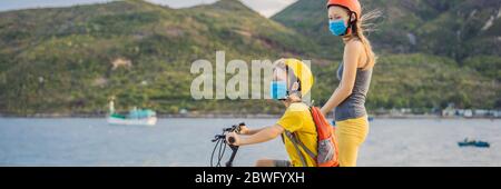 Aktive Schulkind und seine Mutter in medizinischen Maske und Schutzhelm Reiten ein Fahrrad mit Rucksack an sonnigen Tag. Fröhliches Kinderradeln auf dem Weg zur Schule. Sie Stockfoto