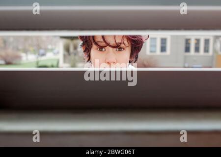 Ein neugieriges Kind, das draußen steht, guckt in den Riss eines Fenster öffnen Stockfoto