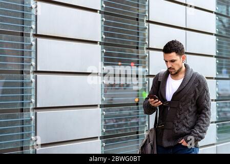 Junger bärtiger Mann, der mit dem Smartphone auf der Straße unterwegs ist Stockfoto
