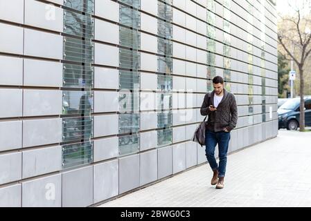 Junger bärtiger Mann, der mit dem Smartphone auf der Straße unterwegs ist Stockfoto