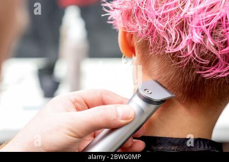 Rückansicht Friseur Hand ist Rasieren rosa Haar der Frau mit elektrischen Trimmer im Friseursalon, Nahaufnahme. Stockfoto