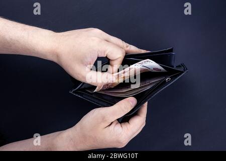 Ein Mann hält eine offene Brieftasche mit Geld in den Händen. Hände nehmen Rechnungen aus seiner Brieftasche. Das Konzept der Ablehnung von Papiergeld, Inflation, FIN Stockfoto