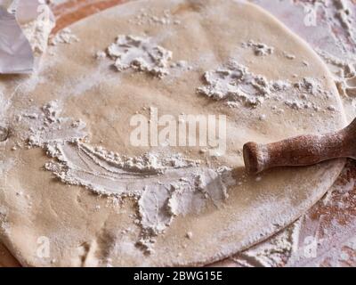 Stück Eiernudelteig ausgerollt auf dem Tisch mit dem Nudelholz. Stockfoto