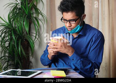 Mann in Gesichtsmaske arbeitet und trinkt Kaffee Stockfoto