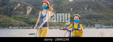 Aktive Schulkind und seine Mutter in medizinischen Maske und Schutzhelm Reiten ein Fahrrad mit Rucksack an sonnigen Tag. Fröhliches Kinderradeln auf dem Weg zur Schule. Sie Stockfoto
