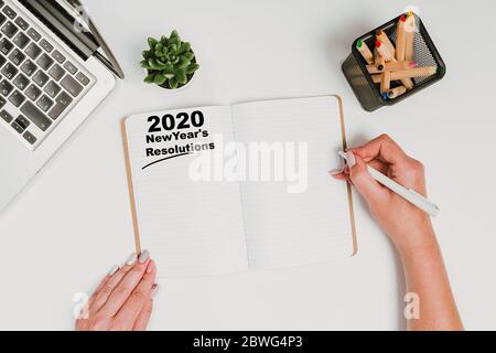 New Year Concept - 2020 Nummer und Text auf Notizblock und weiblichen Händen moderner Arbeitsplatz mit Kaffeetasse, Smartphone, Papier, Notebook, Tablet und Laptop Stockfoto