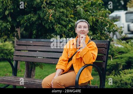 Glücklich stilvolle modische ältere Frau sitzt auf einer Bank in der Stadt Straßen. Anti-Aging-Konzept Stockfoto