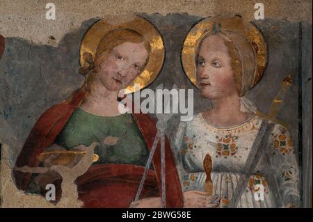 Zwei sizilianische Heilige zeigen Folterinstrumente, die von ihren römischen Verfolgern verwendet wurden, im Detail mit dem Fresko der Spätgotik oder Frührenaissance, der Kirche des hl. Franziskus, in Lucignano, Toskana, Italien. St. Agatha oder Santa Agata (links) hält Scheren oder Zangen und St. Lucy oder Santa Lucia ein Schwert. Stockfoto