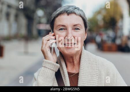 Glückliche ältere Frau auf den Straßen der Stadt mit Handy. Stockfoto