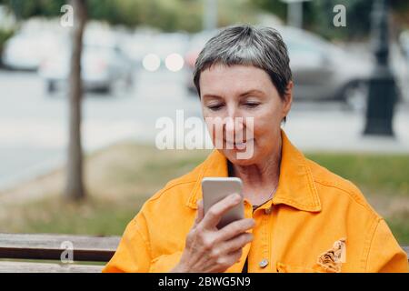Glückliche ältere Frau auf den Straßen der Stadt mit Handy. Stockfoto