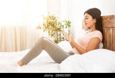 Japanisch Mädchen Mit Handy Texting Sitzen Im Bett Im Schlafzimmer Stockfoto