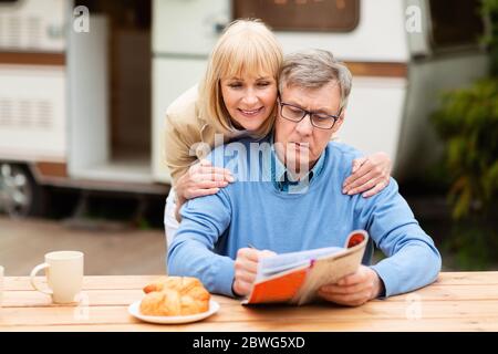 Ältere Frau hilft ihrem Mann lösen Kreuzworträtsel in der Nähe Anhänger im Freien Stockfoto