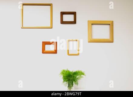 Leere Bilderrahmen an der weißen Wand und Farnblätter in Glas auf dem Tisch Stockfoto