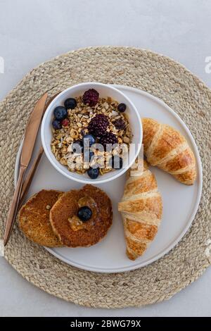 Obere Ansicht von einer gesunden und nahrhaften Frühstücksplatte mit Müsli, Haferflocken Pfannkuchen und Croissants. Stockfoto