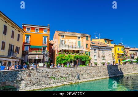 Sirmione, Italien, 11. September 2019: Fußgängerstraßendamm im historischen Stadtzentrum mit Straßenrestaurants und bunten Gebäuden mit bunten Mauern, Wandertouristen, blauem Himmel Stockfoto