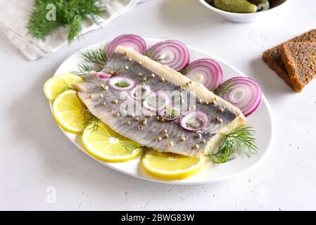 Gesalzener Hering mit Zwiebeln und Zitrone auf weißem Teller, Nahaufnahme. Russische Küche. Stockfoto