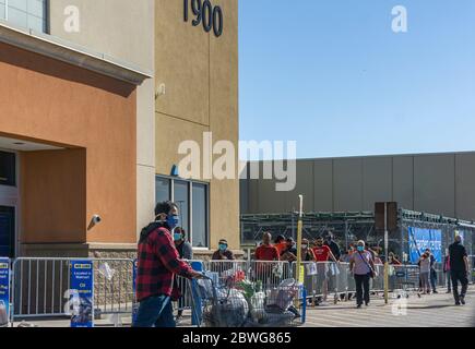 Erwachsene männliche tragen Gesichtsmaske kommt mit einem Wagen mit Lebensmitteln, während andere Käufer warten in der Schlange halten soziale Distanz Stockfoto