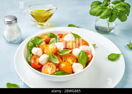 Salat mit gelber Tomatenkirsche und Mini-Mozzarella-Käse in weißer Schüssel auf weißem Teller. Bocconcini Mozzarella Käse mit frischen Basilikumblättern in Stockfoto