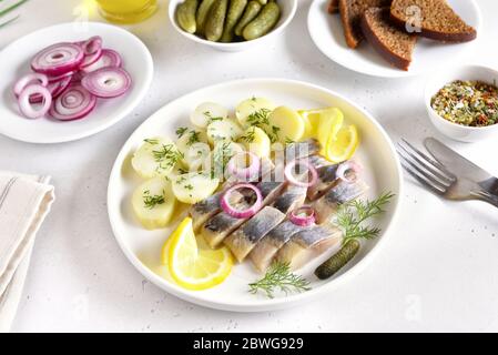 In Scheiben geschnittener Heringsfisch mit gekochten Kartoffeln auf weißem Teller. Russische Küche Stockfoto