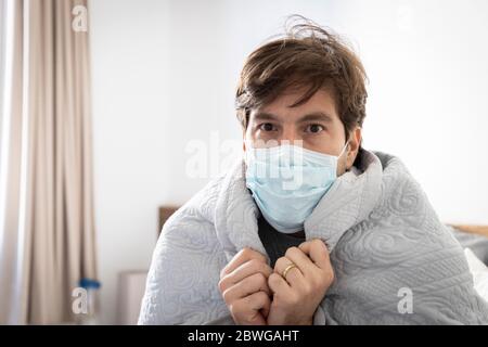 Ein kranker Mann, mit einer Decke über dem Rücken und einer Maske über Mund und Nase. Stockfoto