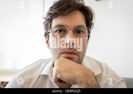 Mann, der direkt auf die Kamera schaut, um ein Konferenzgespräch zu führen, und das Heimbüro zu machen. Stockfoto