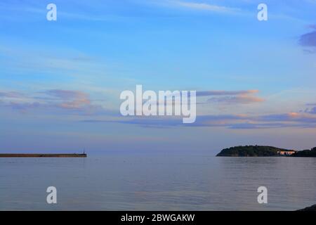 Barry, Wales, der Damm und Punkt auf Barry Island am Horizont. Flut mit Sonnenuntergang und Wolken über dem Himmel verstreut. Stockfoto