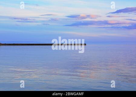 Barry, Wales, der Damm und Punkt auf Barry Island am Horizont. Flut mit Sonnenuntergang und Wolken über dem Himmel verstreut. Stockfoto