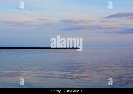 Barry, Wales, der Damm und Punkt auf Barry Island am Horizont. Flut mit Sonnenuntergang und Wolken über dem Himmel verstreut. Stockfoto